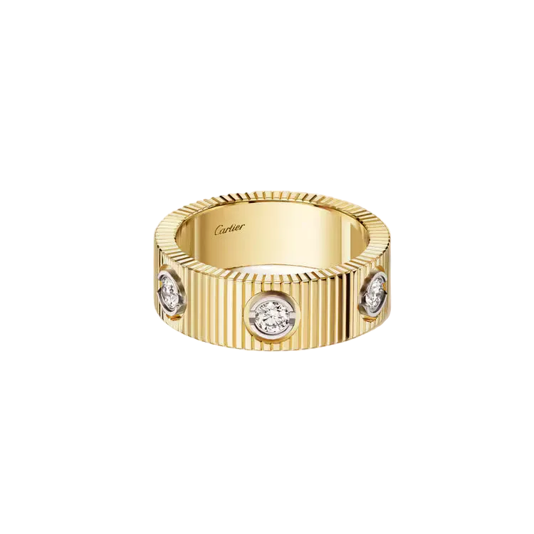 A Cartier gold ring with a vertically ribbed band and three bezel-set round diamonds, photographed on a clean off-white background.