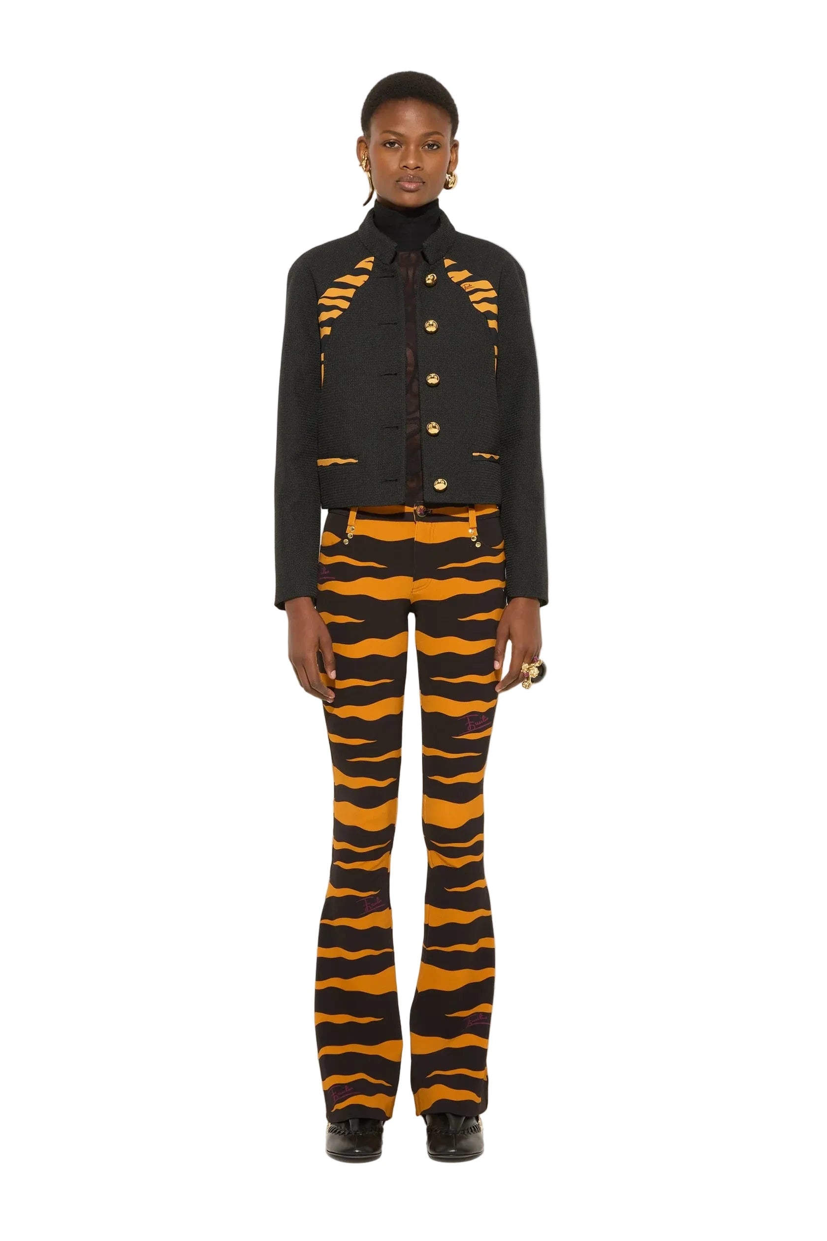 A model stands against a plain white studio background wearing a black jacket with orange tiger-stripe details and matching black-and-orange striped pants.