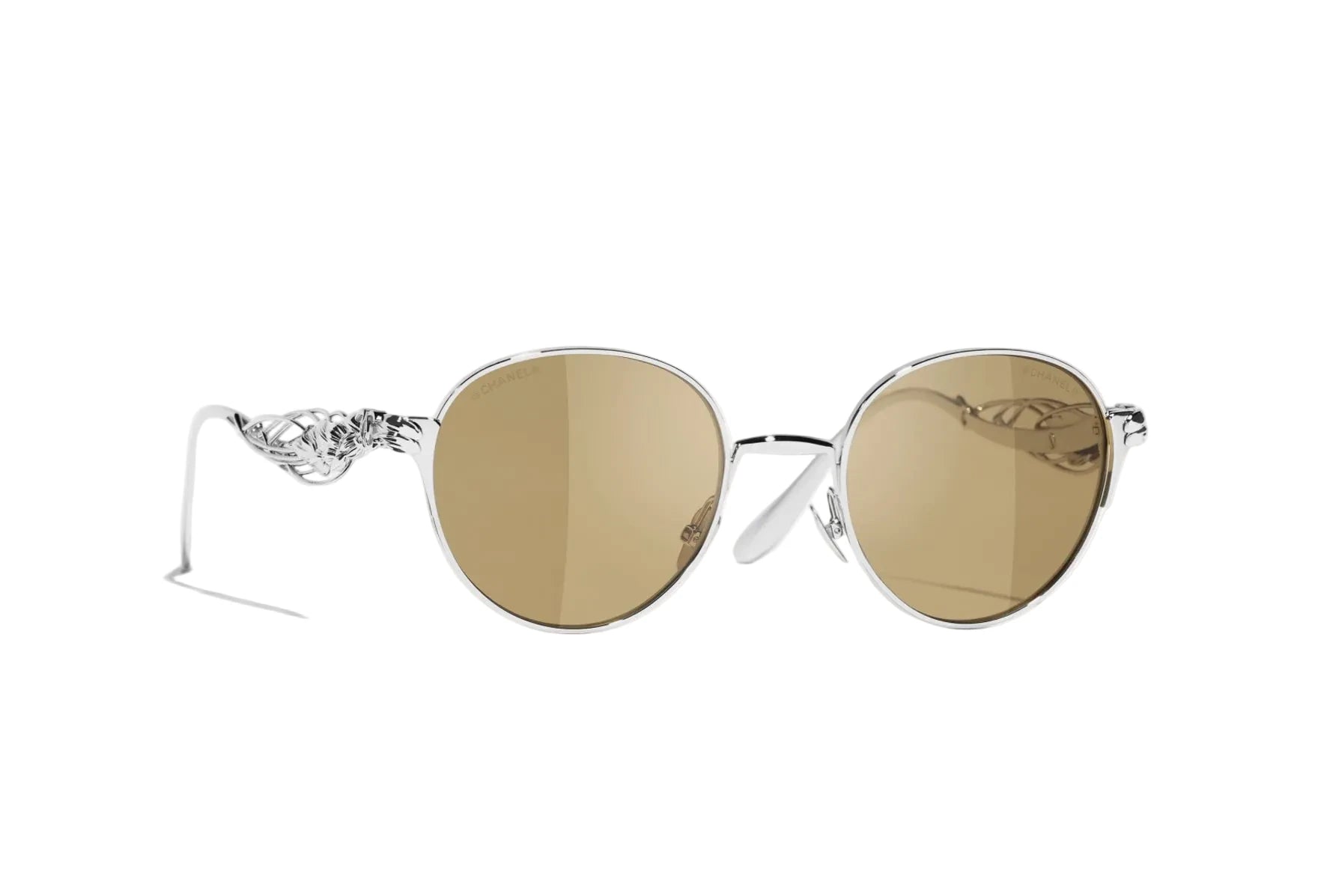 Oval sunglasses with a silver metal frame, ornate winged temple details, and warm brown-tinted lenses, shown on a clean white background.