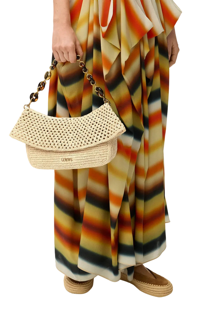 Person holding a beige handbag with a colorful striped dress on a white background