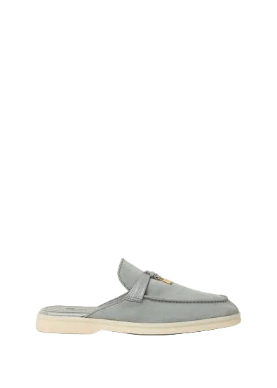 A light gray suede mule loafer with a small gold-tone horsebit detail on the strap, set against a solid off-white background.