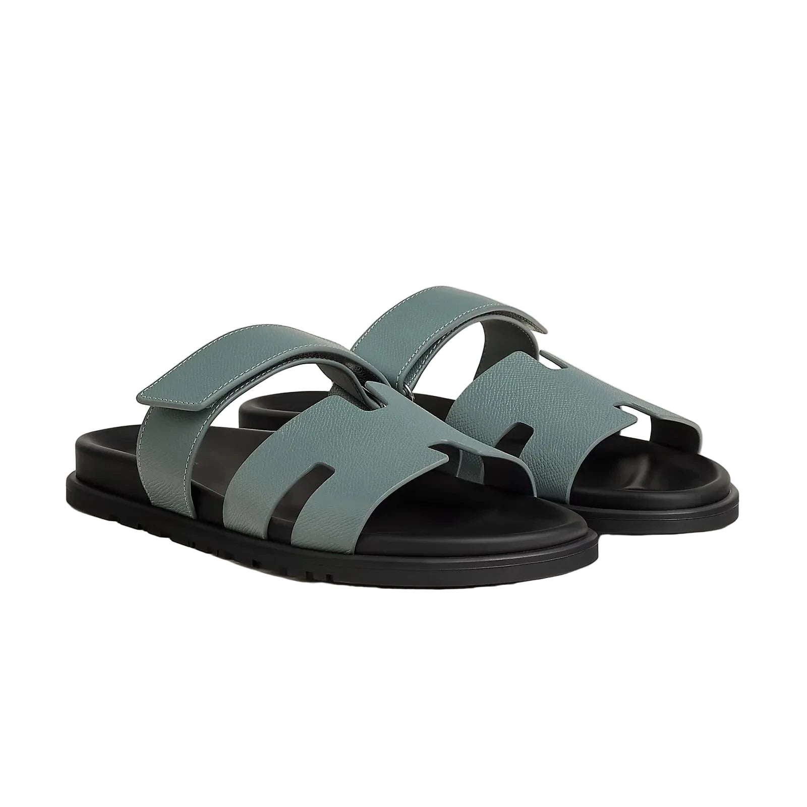 Pair of green sandals with black soles on a light gray background
