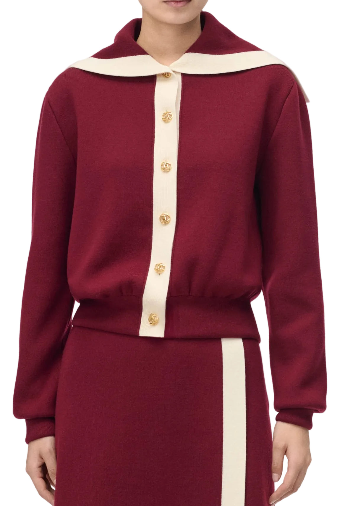 A model wearing a burgundy knit cardigan with a cream collar and cream button placket, paired with a matching skirt.