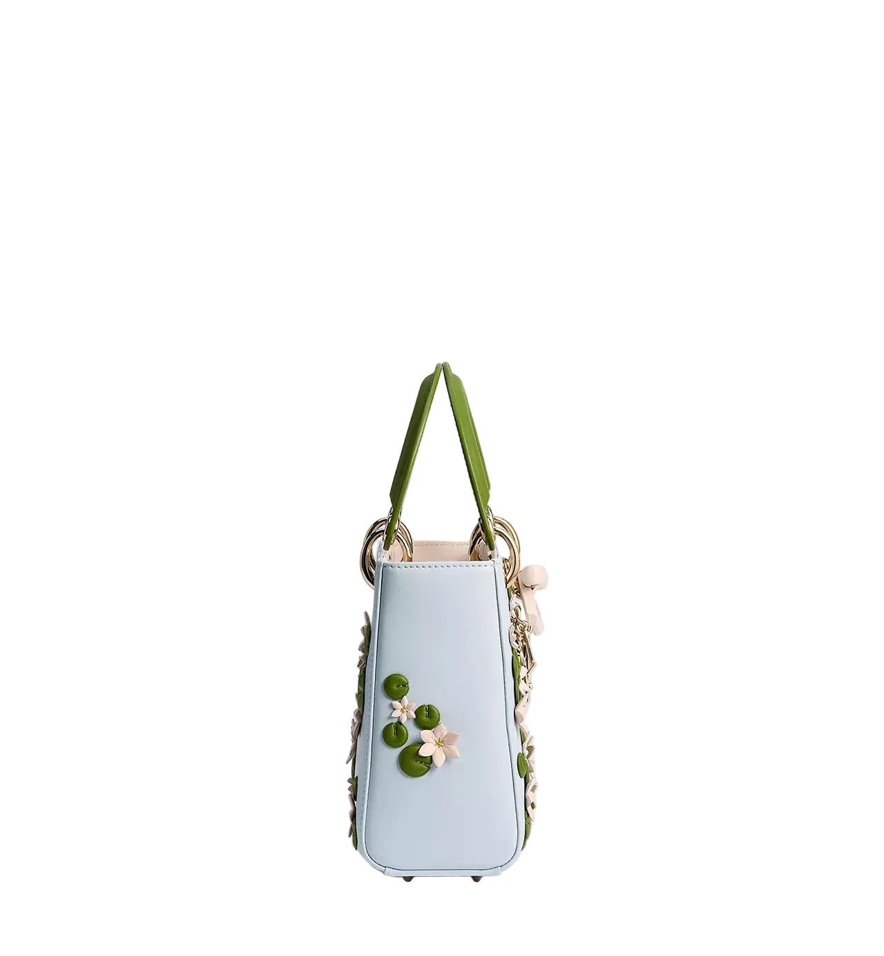 A light blue leather handbag with green handles, decorated with 3D green leaves and white and pink flowers on the front, set against a plain light gray background.