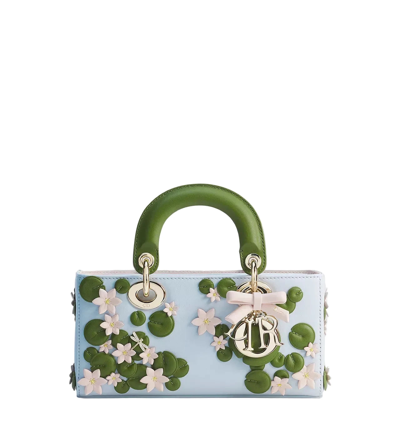A light blue leather handbag with a structured top handle, decorated with 3D green lily-of-the-valley motifs, white flowers, and a gold-tone Christian Dior charm with a pink bow, set against a plain light gray background.