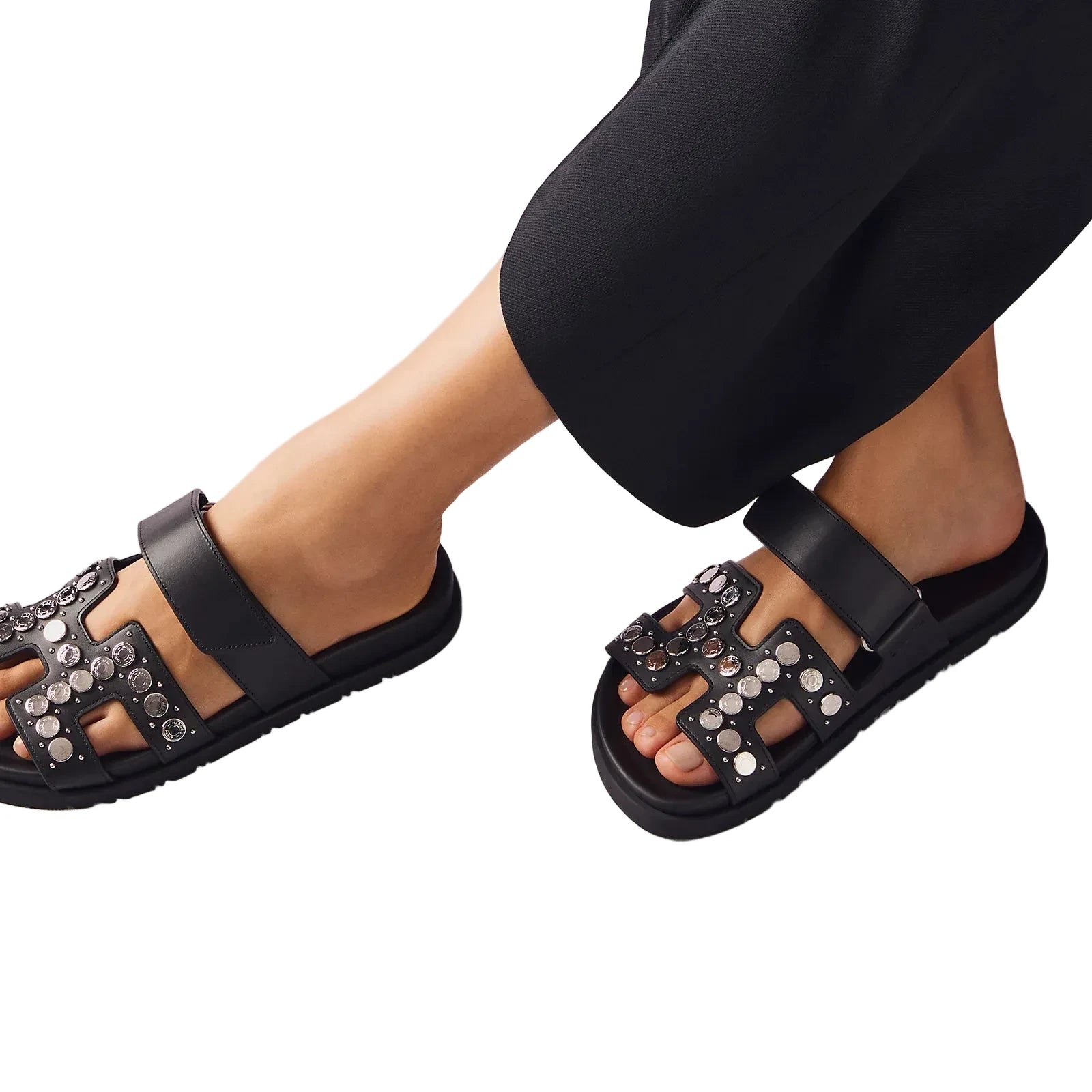 Black sandals with embellishments worn by a person on a light gray background
