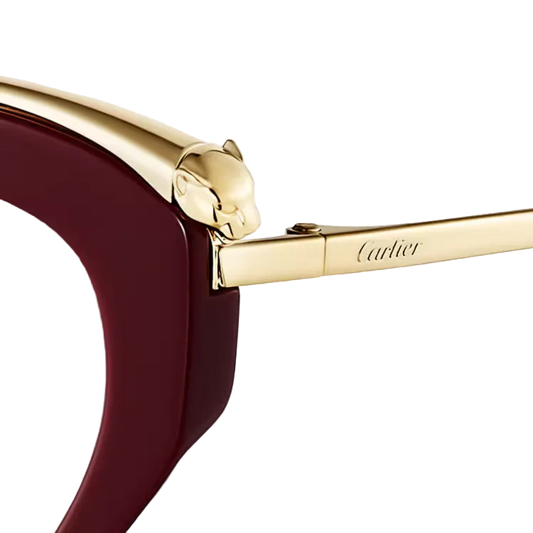 Close-up of Cartier sunglasses showing a deep burgundy acetate frame, a polished gold metal brow piece with a panther head detail, and the Cartier logo engraved on the temple arm against a light off-white background.