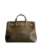 An olive green leather tote bag with a top handle, a front belt detail, and a gold-tone 'CD' logo clasp, photographed on a light gray background.