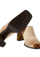 Pair of beige high-heeled shoes with tortoiseshell accents on a light gray background