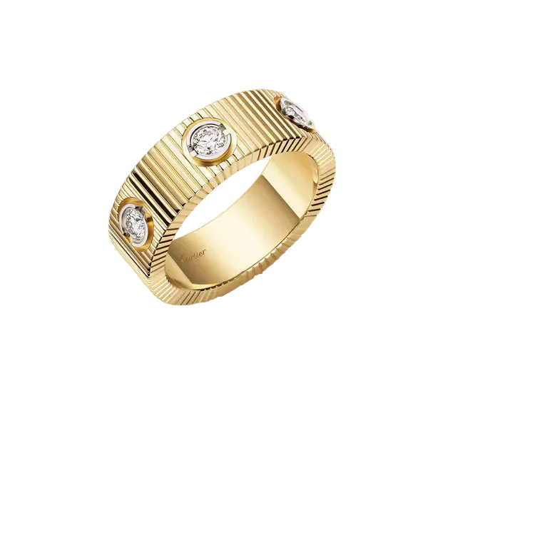 A yellow gold ring with a ribbed textured band and three bezel-set round diamonds, shown on a clean off-white background.