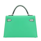 Green handbag with black handle on a light gray background