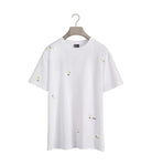 White t-shirt with small embroidered designs on a hanger against a white background
