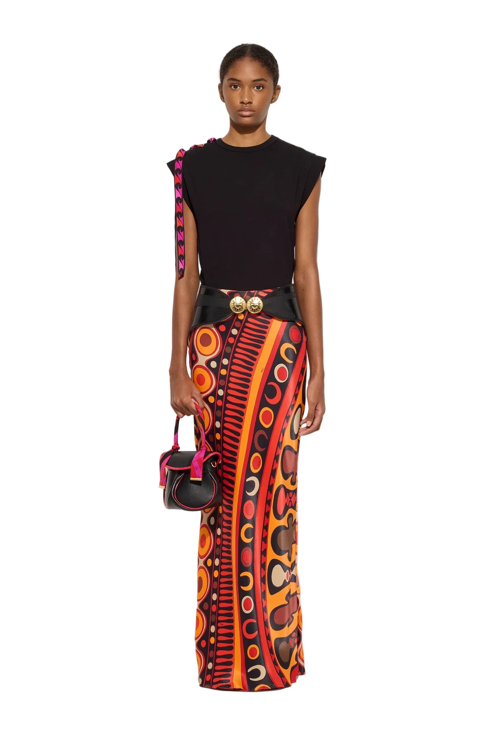 Model wearing a black sleeveless top and colorful patterned skirt with a handbag on a white background