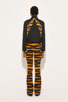 A model shown from the back wearing a black cropped jacket with a bold orange and black tiger-stripe pattern on the back, paired with matching patterned flared pants, against a plain white studio background.