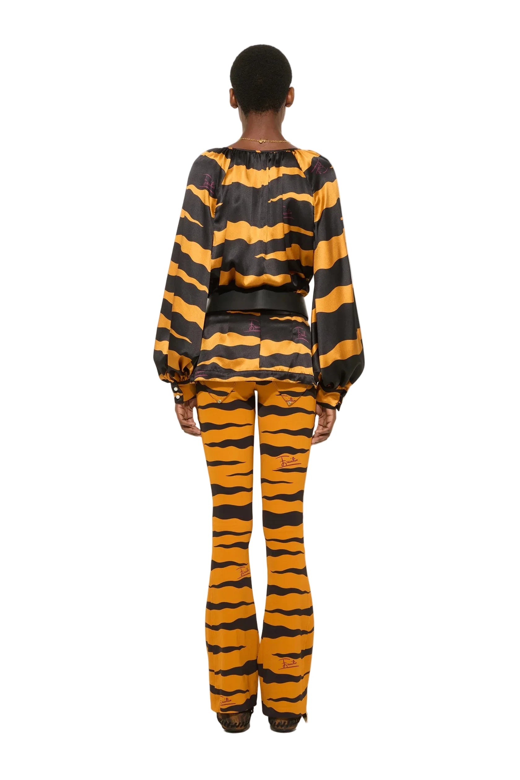 A model viewed from the back wearing a matching tiger-print top and flared pants set in orange and black, standing against a plain white studio background.