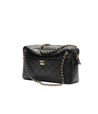 Black quilted handbag with gold chain and hardware on a white background