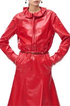 A model wearing a shiny red faux-leather long-sleeve shirt dress with a ruffled collar, button front, and a matching red belt, shown against a plain light background.