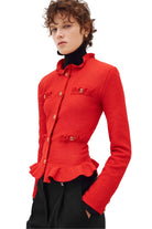A model wearing a bright red textured tweed jacket with gold-tone decorative buttons and a high ruffled collar, paired with a black turtleneck and black trousers, against a plain white studio background.