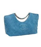 A blue suede Chanel hobo bag with a chain shoulder strap and an embossed CC logo on the front, photographed on a clean white background.