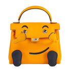 Bright yellow handbag with a playful cartoon face design, featuring black embroidered eyebrows, eyes, mouth, and black paw-print feet, shown on a plain white background.