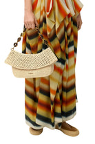Person holding a beige handbag with a colorful striped dress on a white background