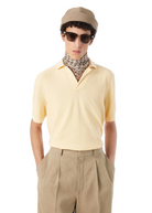 Man wearing a light yellow polo shirt, beige cap, sunglasses, and patterned scarf on a white background