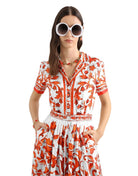 Woman wearing a red and white floral dress with sunglasses on a light gray background