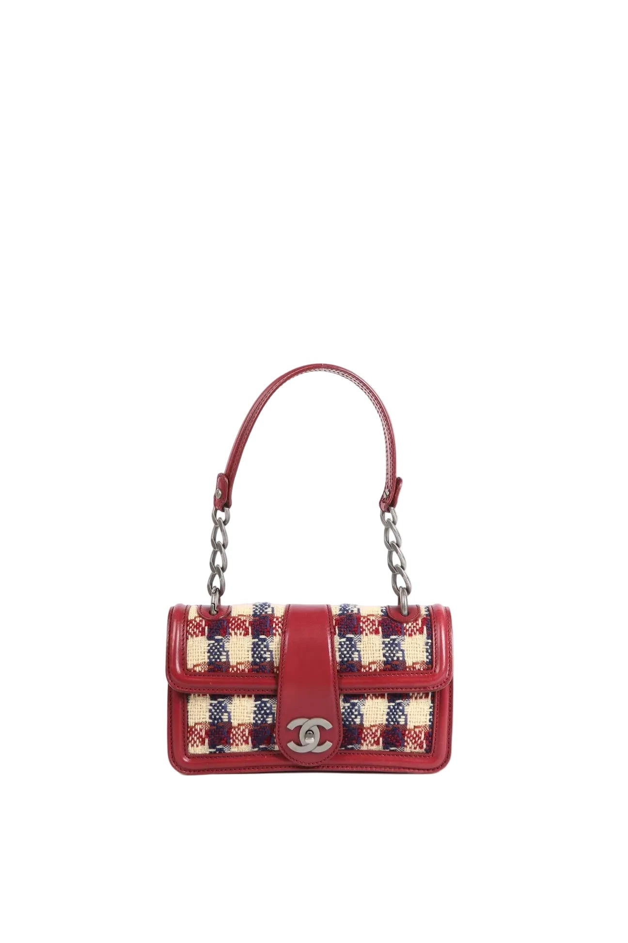 A Chanel shoulder bag featuring a red leather body, a top handle, and a woven tweed body with a red, beige, and navy plaid pattern. The bag has a silver-tone interlocking CC logo on the front flap.