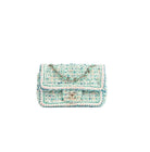 A small tweed shoulder bag in light blue, white, and beige with a gold-tone chain strap and a gold interlocking CC logo on the front flap, photographed on a clean white background.