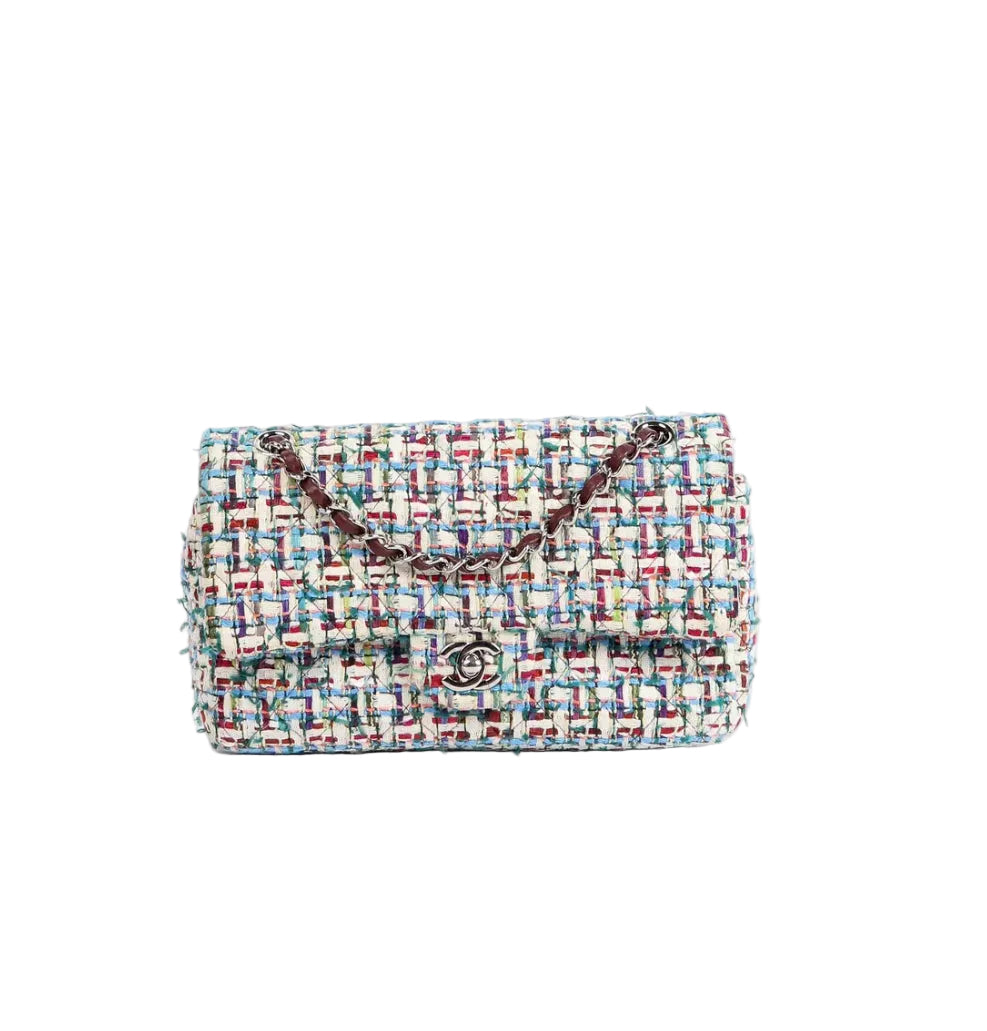 A Chanel tweed flap bag in a multicolor blue, red, and cream bouclé weave, featuring a dark brown chain strap and a silver-tone interlocking CC logo clasp on a white background.