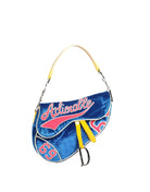 A blue velvet saddle-style handbag with a yellow leather handle, featuring 'Actionable' in red script and the number '65' in red on a white background.