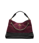 A Chanel hobo handbag in deep burgundy quilted suede and black quilted leather, featuring a gold-tone interlocking CC logo and a gold chain strap on a white background.