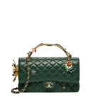 A dark green quilted leather handbag with gold-tone hardware, featuring decorative embroidered flowers, a twisted top handle, and a gold chain strap, photographed against a plain white background.