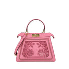 A pink leather handbag with a top handle, gold-tone hardware, and a decorative laser-cut floral panel on the front, photographed against a plain light gray background.