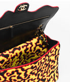 Chanel handbag with black interior and yellow leopard print exterior on a white background