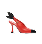 Red high-heeled shoe with black cap-toe and decorative bow on a white background