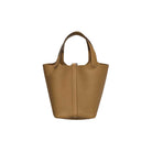 A tan pebbled leather handbag with dual top handles and a vertical front strap detail, shown against a plain light gray background.
