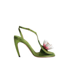 An olive green peep-toe high heel sandal with a T-strap, ankle buckle, and a decorative pink and white flower embellishment on the toe, shown against a plain light gray background.