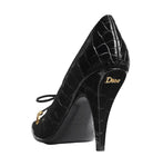 Black high-heeled shoe with crocodile texture and Dior logo on a light gray background