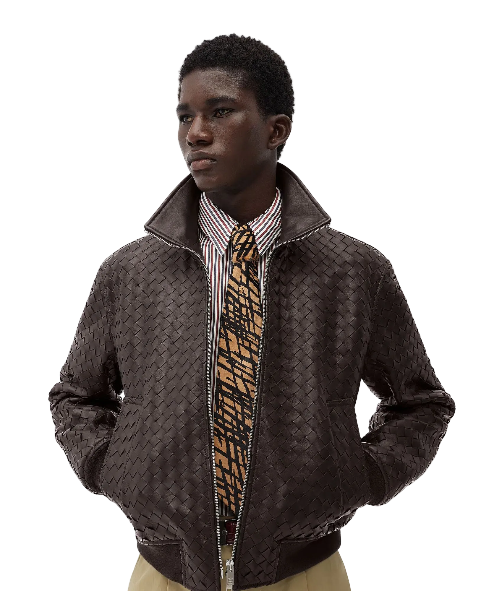A male model wearing a dark brown woven leather bomber jacket over a striped shirt and a patterned tie, photographed against a light gray studio background.