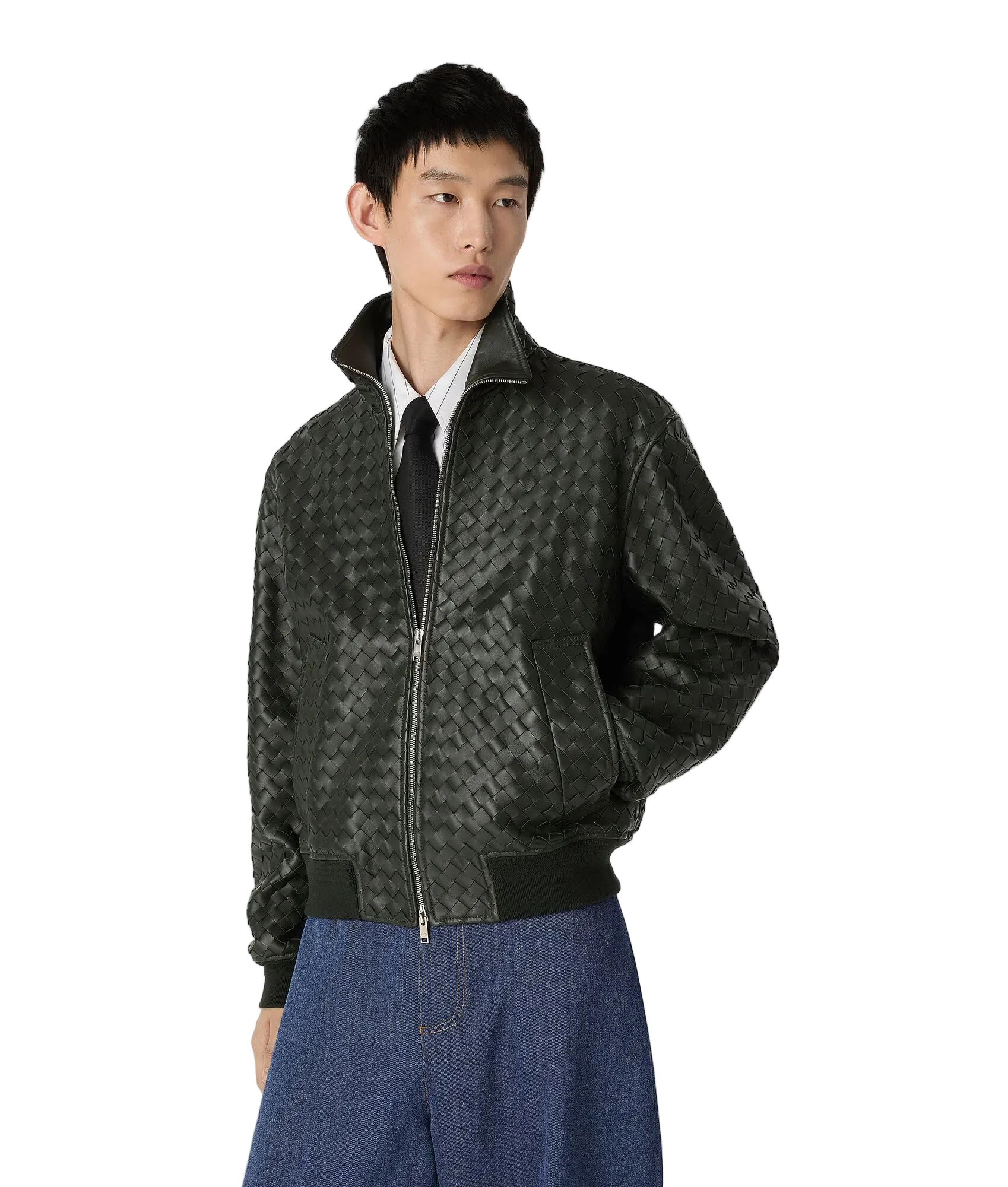 A male model wearing a dark green textured zip-up bomber jacket over a white collared shirt and black tie, paired with blue jeans, against a light gray studio background.