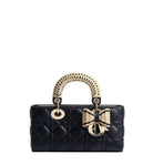 Black quilted handbag with gold handle and bow on a light gray background