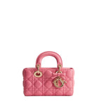 A pink quilted leather top-handle handbag with gold-tone hardware, including a bow detail and a hanging CD charm, photographed against a clean white background.