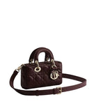 A dark burgundy quilted leather handbag with gold-tone hardware, featuring a top handle, a detachable shoulder strap, and a hanging Christian Dior logo charm, photographed on a light gray background.