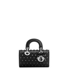 A black leather handbag with silver-tone hardware, featuring a scalloped edge, a polka-dot pattern, a top handle, and a decorative bow with a metal clasp on a light gray background.