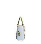 A light blue leather handbag with green handles, decorated with 3D green leaves and white and pink flowers on the front, set against a plain light gray background.