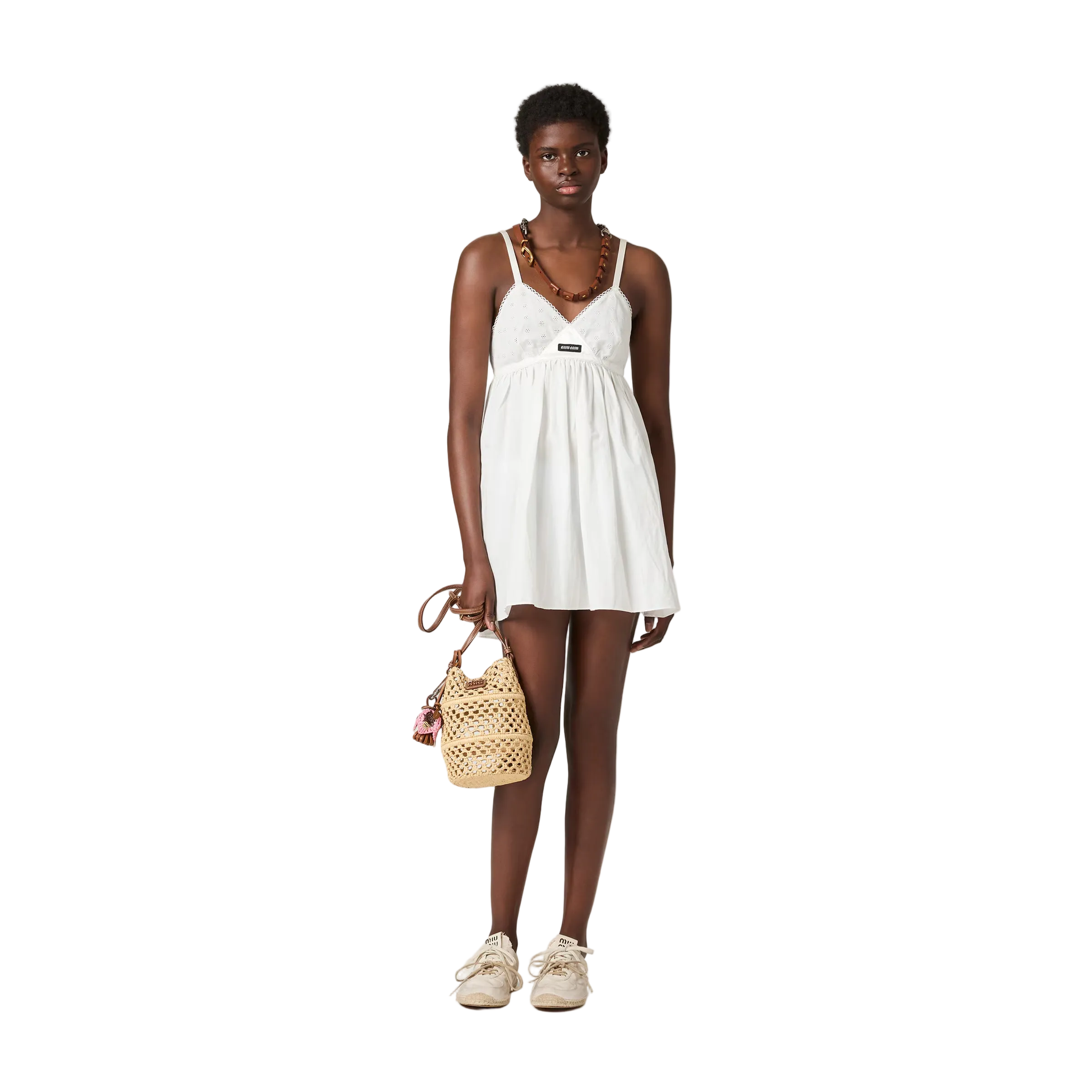 Woman wearing a white dress holding a woven handbag on a beige background