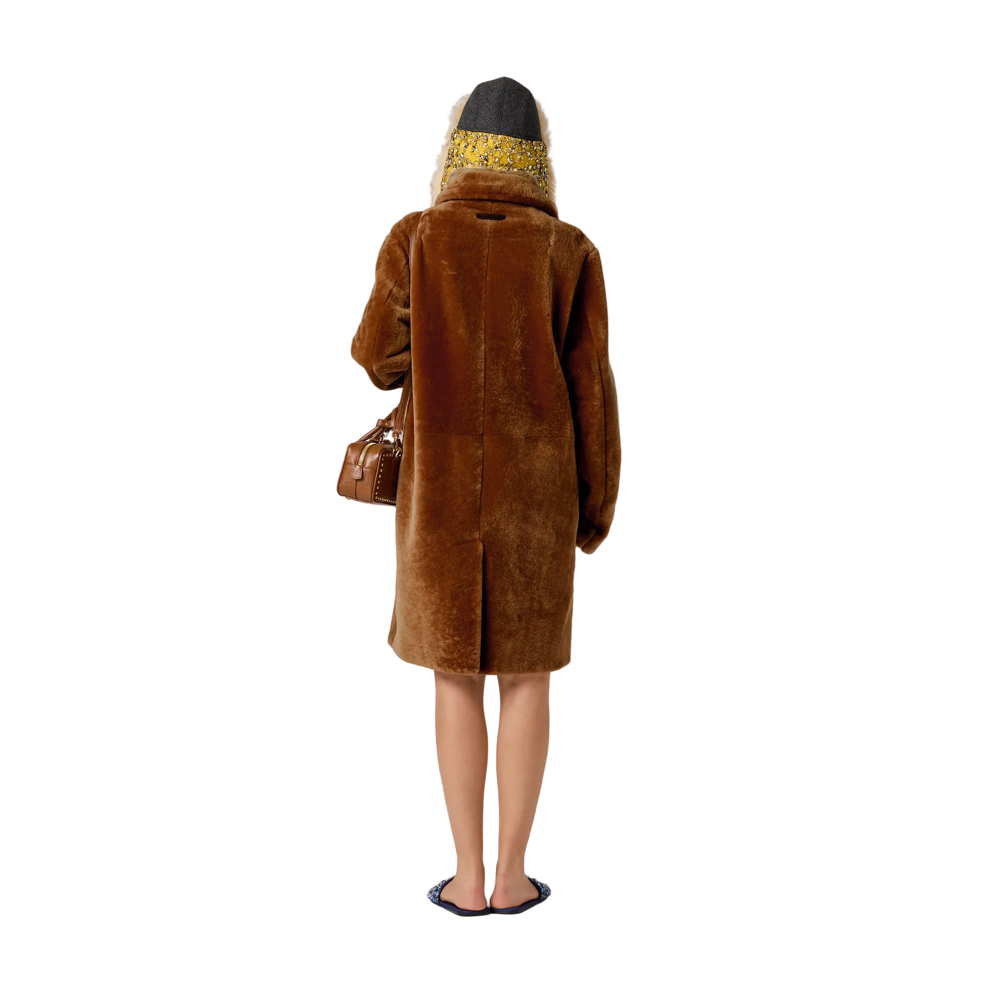 A model shown from behind wearing a brown teddy coat, a patterned yellow and black headscarf, and carrying a brown leather handbag against a solid light beige background.