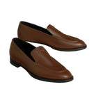 A pair of men's brown leather slip-on loafers with a subtle embossed logo on the vamp, displayed on a light beige background.