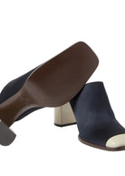 Navy blue suede mules with brown and beige heels on a light gray background